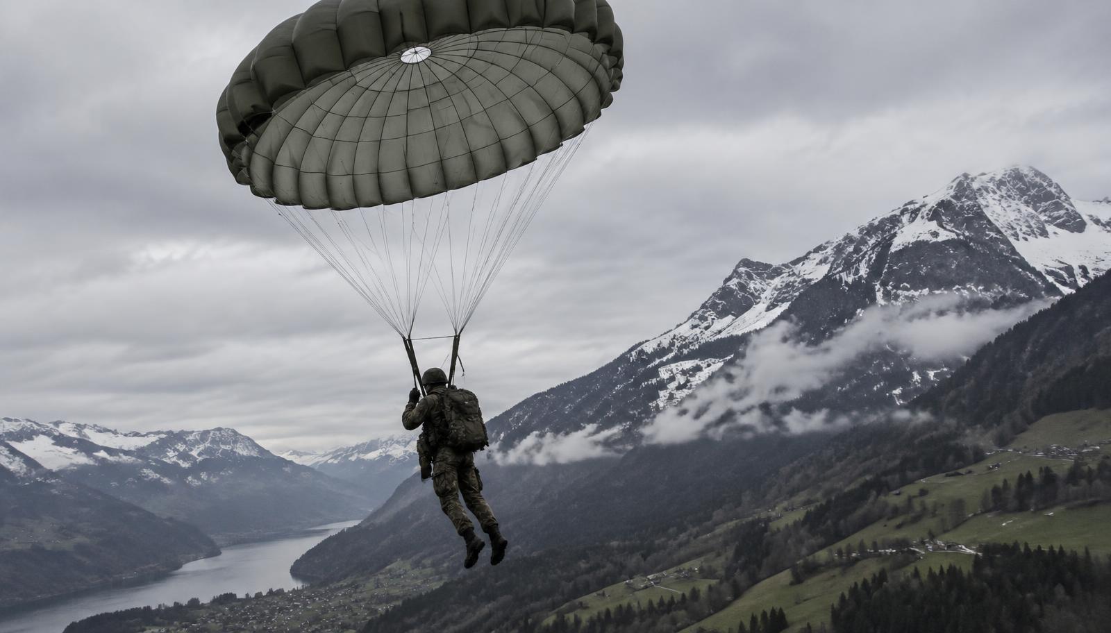 Militärischer Fallschirmspringer unter geöffneter Rundkappe im Anflug auf ein Absetzgelände in den Schweizer Alpen.