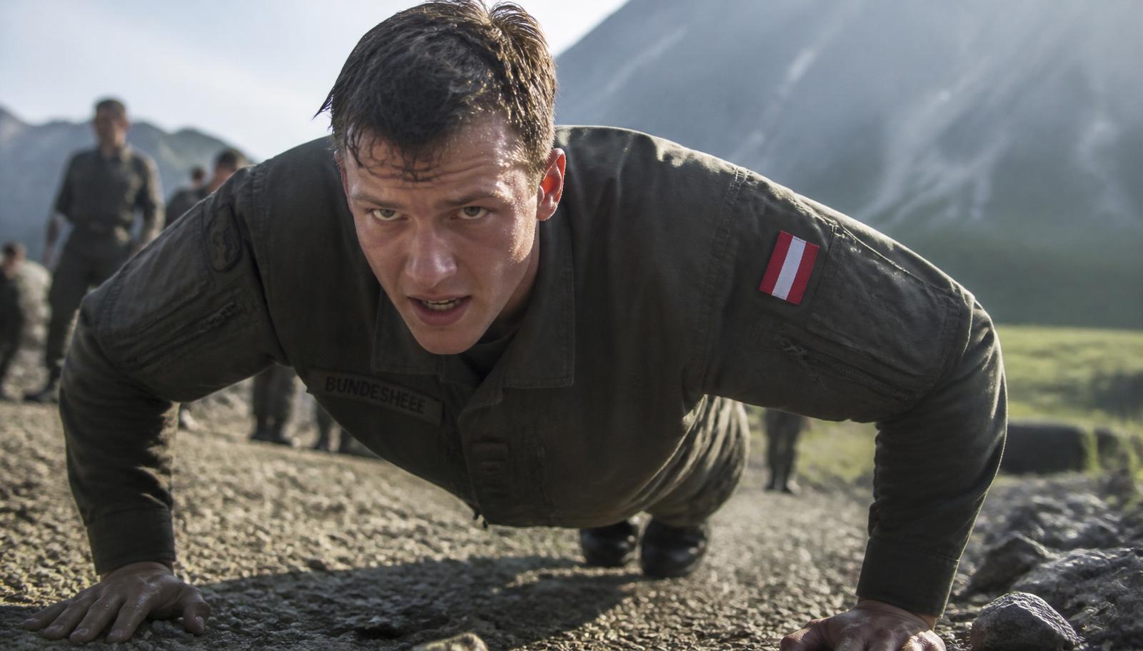 Junger Bundesheer-Soldat in olivgrüner Feldbluse absolviert Liegestütz auf Schotter im alpinen Gelände.