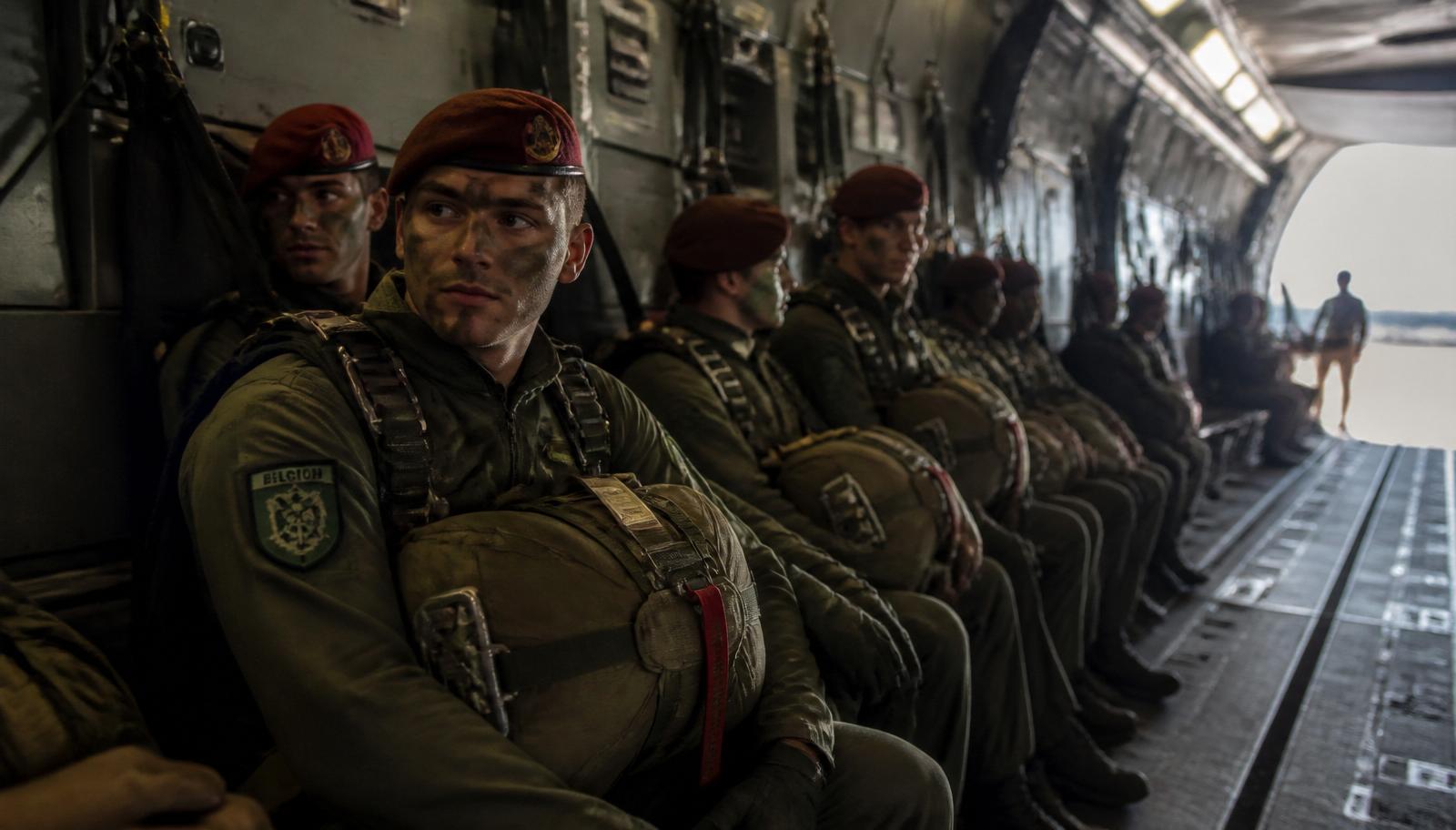 Belgische Para-Commandos in olivgrünen Uniformen mit rotem Barett und Fallschirm-Rucksack sitzen im Frachtraum eines Airbus A400M kurz vor dem Absprung.